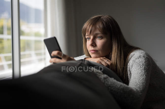 Femme utilisant un téléphone portable dans le salon à la maison — Photo de stock