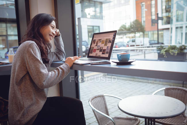 Hermosa mujer usando el ordenador portátil mientras toma café en la cafetería - foto de stock