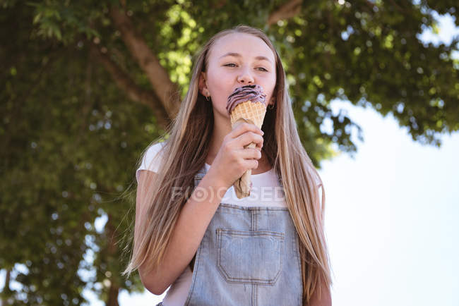Primer plano de la niña comiendo helado bajo el dosel del árbol . - foto de stock