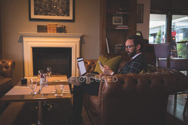 Empresário usando laptop e telefone celular no quarto de hotel — Fotografia de Stock