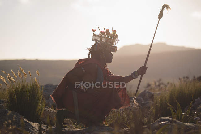 Maasai homem em roupas tradicionais sentado no campo em um dia ensolarado — Fotografia de Stock