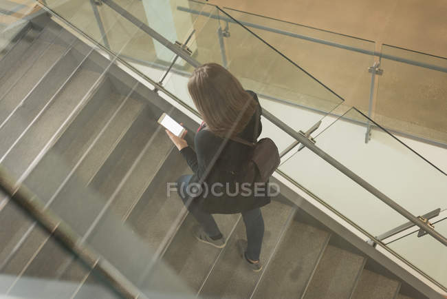 Высокоугольный вид студента колледжа с помощью мобильного телефона на лестнице — стоковое фото