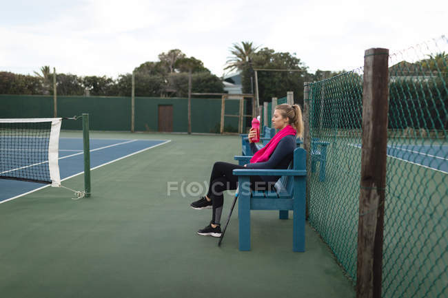 Jeune femme boire de l'eau dans le court de tennis — Photo de stock