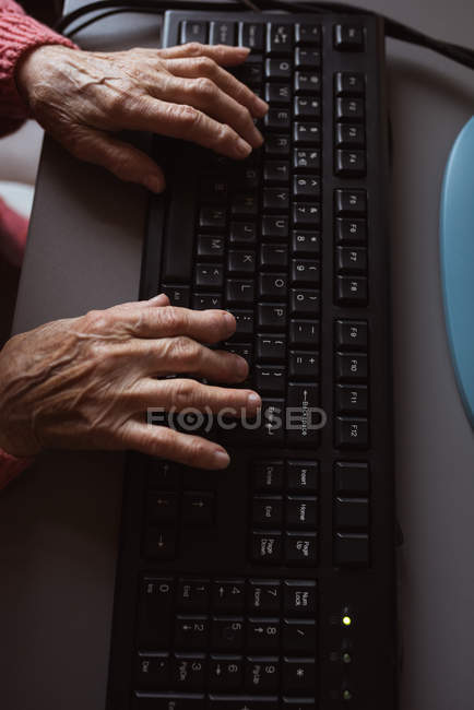 Senior woman tying on keyboard at nursing home — Stock Photo