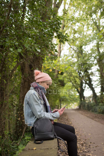 Jovem mulher em roupas quentes usando seu telefone celular no parque — Fotografia de Stock