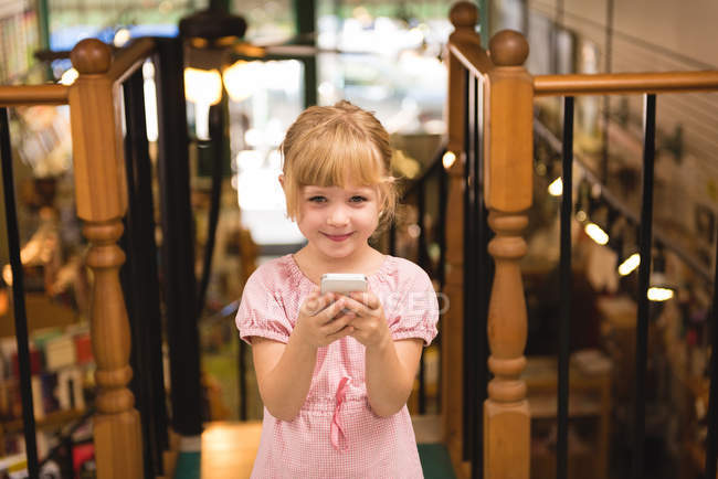 Портрет симпатичной девушки с помощью мобильного телефона в книжном магазине — стоковое фото