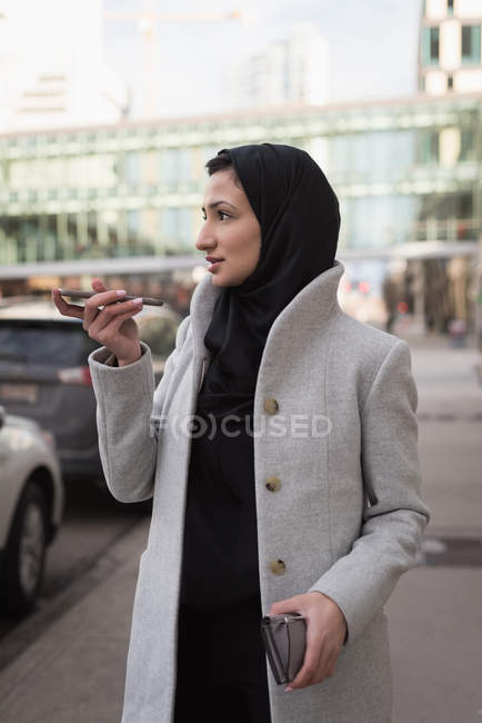 Mujer en hijab hablando por teléfono móvil en la calle de la ciudad - foto de stock