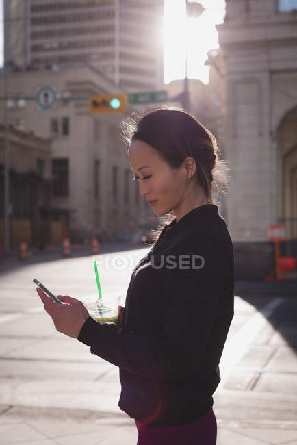 Mulher usando telefone celular enquanto bebe na rua — Fotografia de Stock