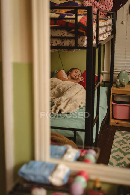 Girl reading book while lying on bed in bedroom at home. — Stock Photo