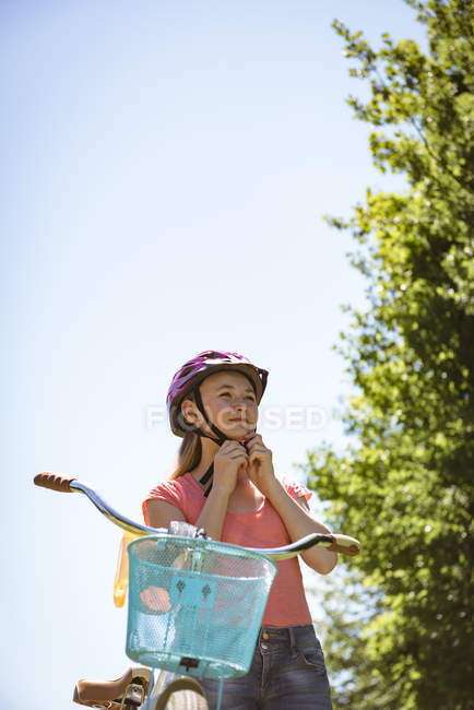Menina com capacete em pé além de bicicleta no país . — Fotografia de Stock