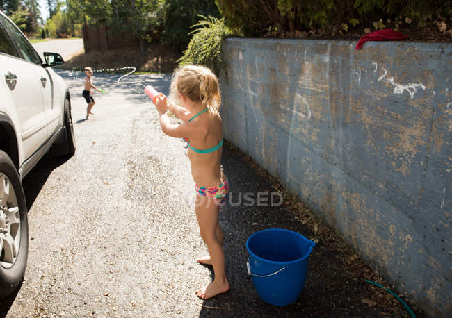 Hermanos jugando con pistola de agua en el garaje exterior - foto de stock