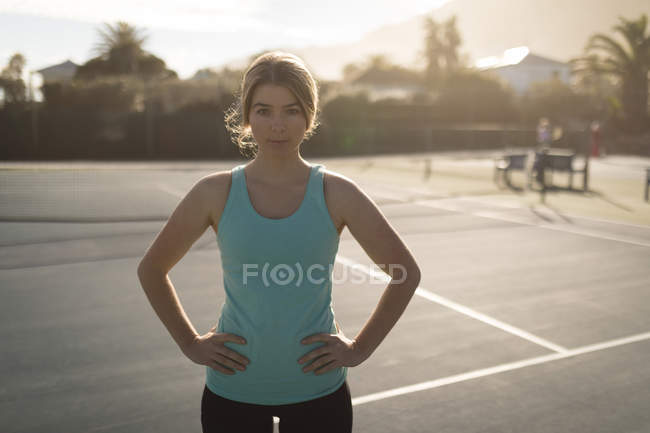 Junge Frau steht mit den Händen an der Hüfte auf dem Tennisplatz — Stockfoto