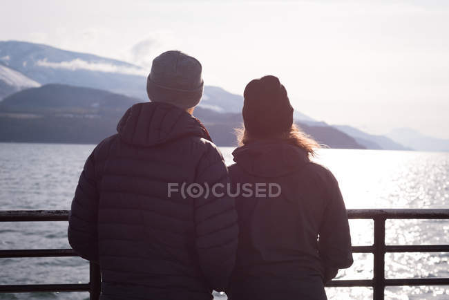 Casal olhando para o rio de pé perto do rio durante o inverno — Fotografia de Stock