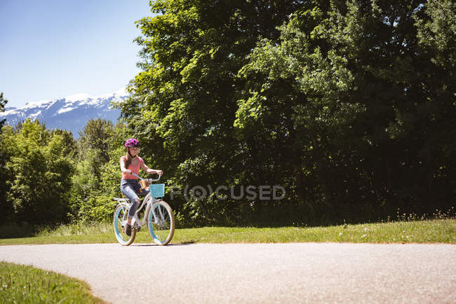 Дівчина в шоломі безпеки їзда на велосипеді по сільській дорозі . — стокове фото