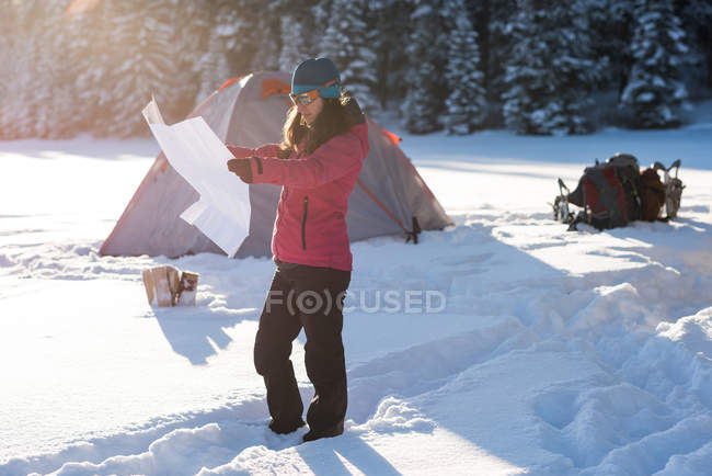 Turista femenina mirando el mapa en un bosque nevado por tienda . - foto de stock