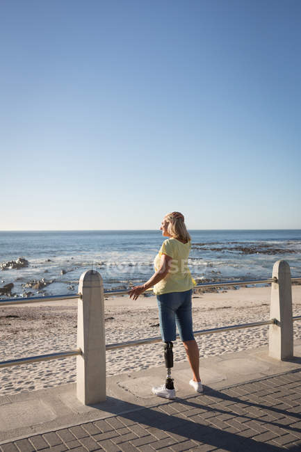 Disabled woman standing by railing at beach. — Stock Photo