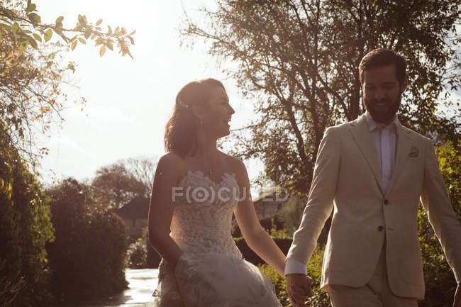 Mariée heureuse et marié marchant main dans la main dans le jardin — Photo de stock