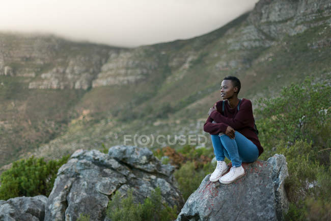 Mujer joven sentada en una roca en el campo - foto de stock