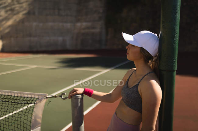 Молодая женщина, опирающаяся на столб на теннисном корте — стоковое фото