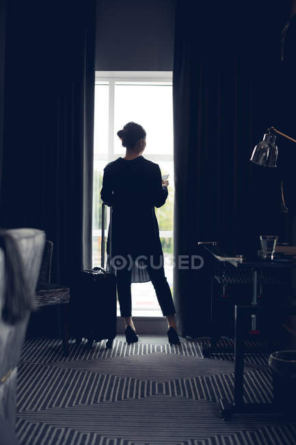 Vue arrière de la femme utilisant le téléphone portable dans la chambre d'hôtel — Photo de stock