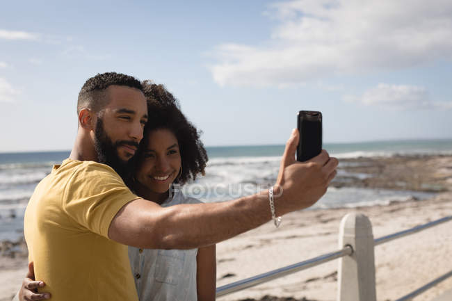Romantisches Paar macht an einem sonnigen Tag Selfie mit Handy in Strandnähe — Stockfoto