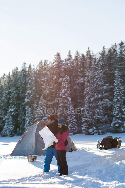 Paar schaut im Winter auf Karte in verschneiter Landschaft. — Stockfoto