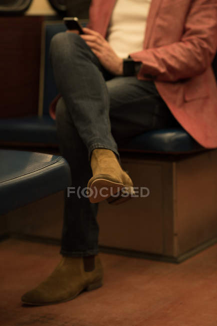 Baixa seção de homem usando telefone celular enquanto viaja no trem — Fotografia de Stock