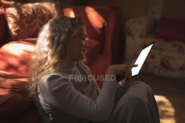Femme mûre assise sur le sol et utilisant sa tablette à la maison — Photo de stock