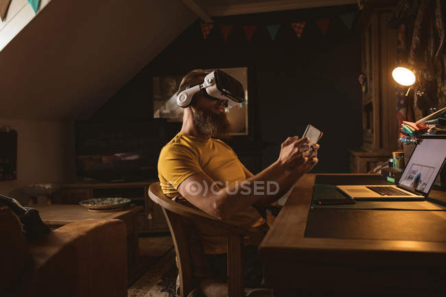 Чоловік в гарнітурі віртуальної реальності, використовуючи свій мобільний телефон вдома — стокове фото