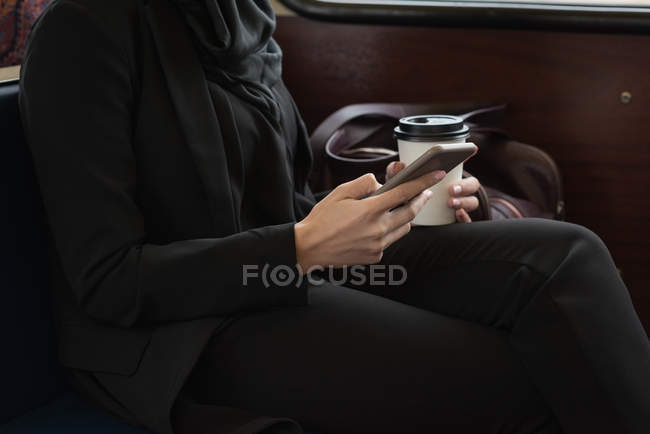 Sección media de la mujer en hijab usando el teléfono móvil mientras viaja en tren - foto de stock