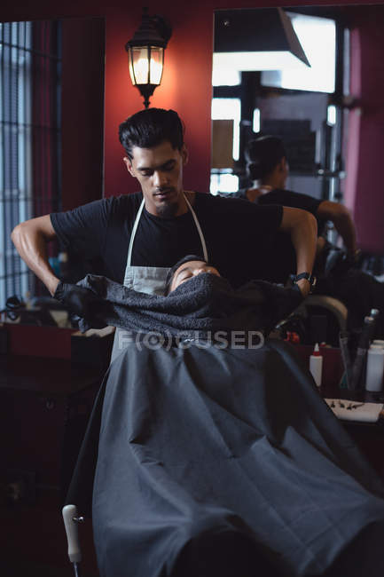 Barber wiping clients face with towel at barbershop — Stock Photo