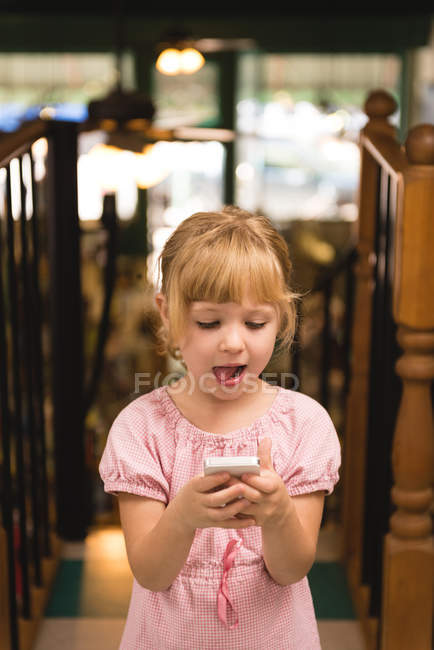 Menina bonito usando telefone celular na livraria — Fotografia de Stock