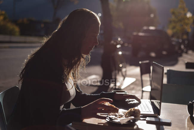 Mulher usando laptop enquanto toma café da manhã no café ao ar livre — Fotografia de Stock
