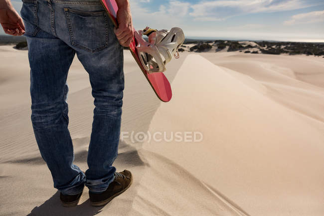 Low section of man with sandboard standing in the desert — Stock Photo