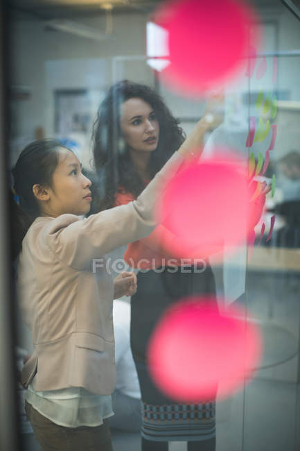 Female executives discussing over sticky notes in modern office — Stock Photo
