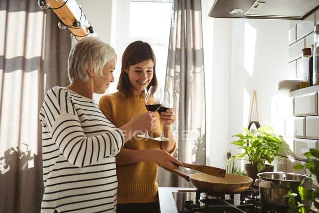 Seniorin und Tochter stoßen beim Kochen in der Küche auf ein Glas Wein an — Stockfoto