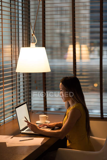 Бізнес-леді використовує свій мобільний телефон під час роботи на ноутбуці в офісі — стокове фото