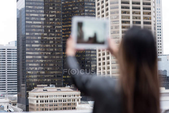 Rückansicht einer Geschäftsfrau, die Wolkenkratzer mit ihrem Tablet fotografiert — Stockfoto