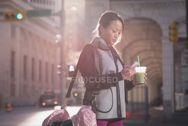 Mujer usando el teléfono móvil mientras bebe en la calle - foto de stock