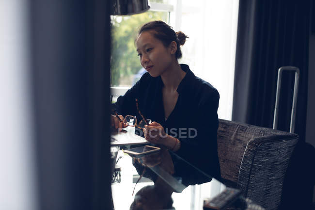 Mujer pensativa sentada con gafas a la mesa en el hotel - foto de stock