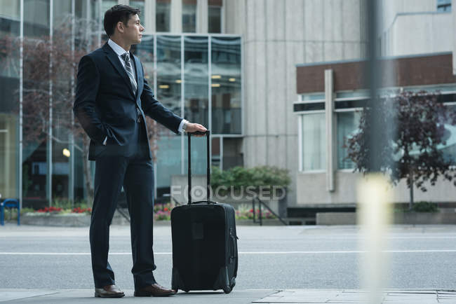 Empresario con maleta en la calle parado fuera del edificio - foto de stock