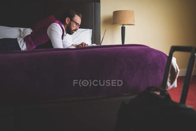 Businessman using laptop on bed in hotel — Stock Photo