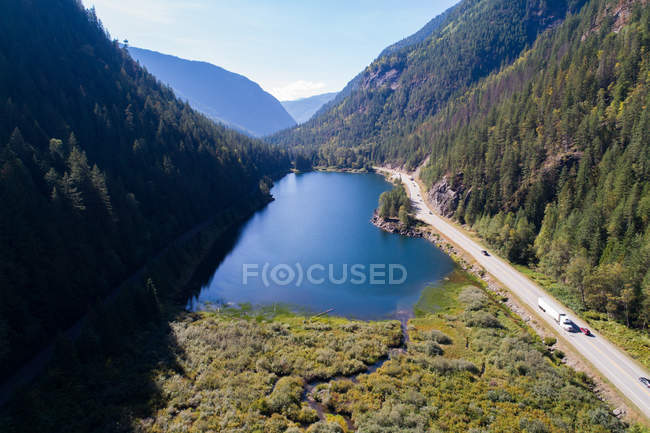 Высокий угол обзора озера и дороги среди покрытых лесом гор — стоковое фото