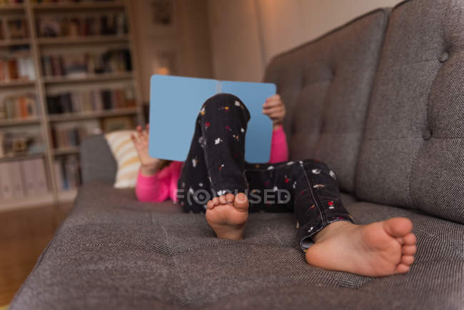 Fille couchée sur le canapé et utilisant une tablette numérique dans le salon à la maison — Photo de stock