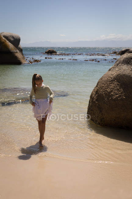 Fille jouer dans l'eau à la plage par une journée ensoleillée — Photo de stock