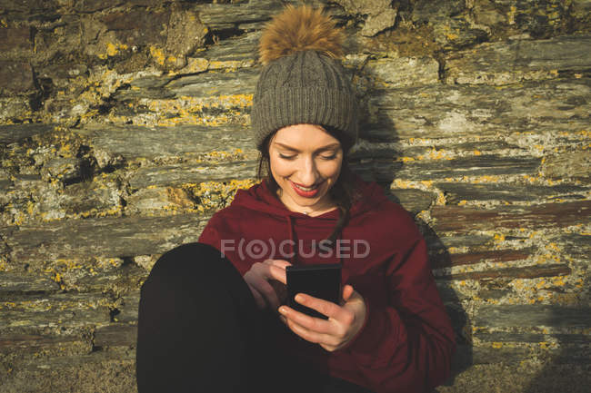 Жінка використовує мобільний телефон проти кам'яної стіни на сонячному світлі . — стокове фото