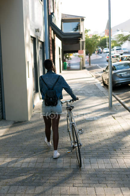 Rear view of woman walking with her bicycle on a sidewalk — Stock Photo