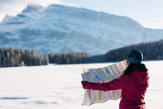 Vue arrière de la femme regardant la carte dans un paysage de montagne enneigé . — Photo de stock