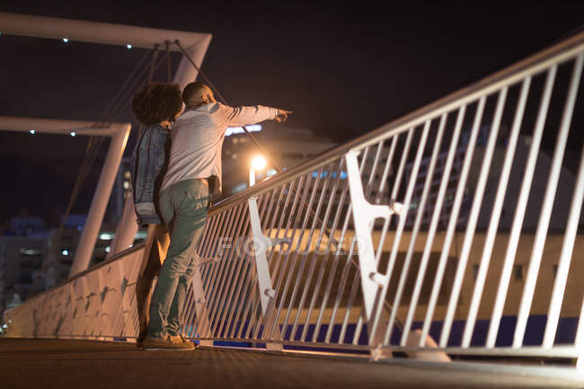 Couple romantique pointant à distance tout en se tenant près de la rampe la nuit — Photo de stock
