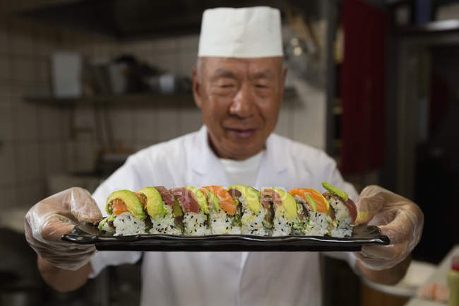 Chef sênior segurando bandeja de sushi na cozinha do hotel — Fotografia de Stock